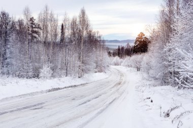 Kış yolu karla kaplı ormanda gün batımında ufukta dağlarla