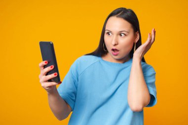 Akıllı telefon kullanan ve gülümseyen genç bir kadın. Sarı arka planda.