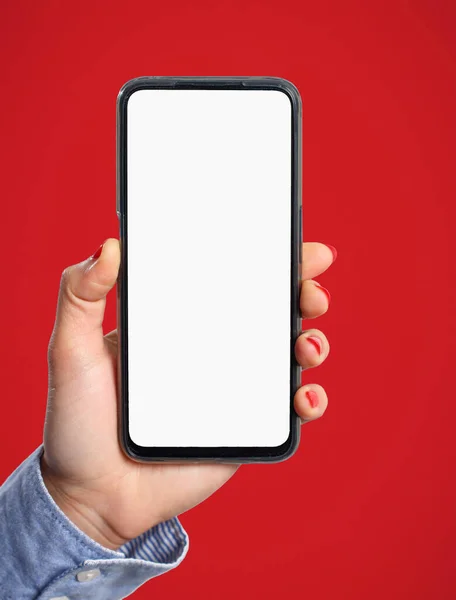 Bir kadının eli dikey olarak kırmızı arka planda beyaz ekranı olan bir akıllı telefonu tutar. Boşluk için.