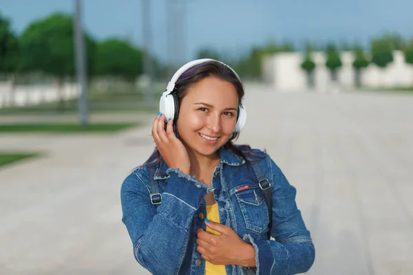 Woman in headphones. Emotional young woman in headphones listening music outdoors