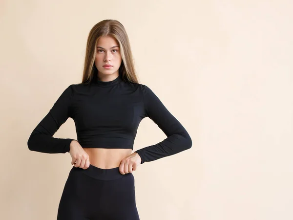 Bej bir arka planda siyah spor giyimli ince bir fitness kadınının portresi.