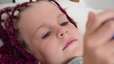 At kuyruklu bir kız yatakta uzanıyor ve cep telefonuyla oynuyor. İletişim araçları. Cep telefonuna bağımlılık kavramı