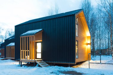 Barnhouse tarzı evler karla çevrilidir. İyi akşamlar, pencerelerden gelen sıcak ışık. Samimi ve sakin bir resim.