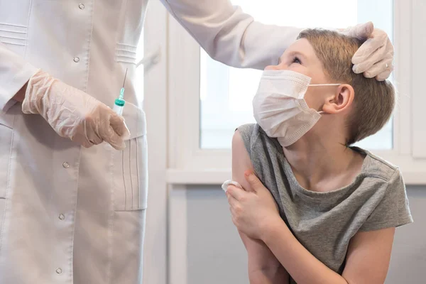 L'enfant remercie le médecin après la vaccination. Le médecin caresse l'enfant sur la tête. Un enfant dans un masque médical regarde le médecin. Protection contre le coronavirus — Photo