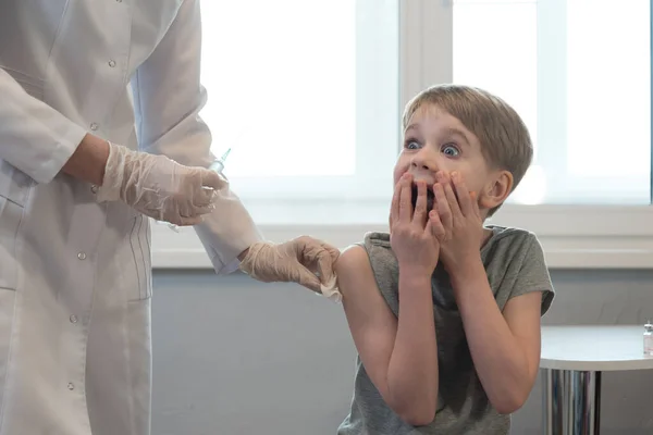 L'enfant regarde la seringue avec horreur. Peur de l'injection. Émotions, réticence à se faire vacciner — Photo