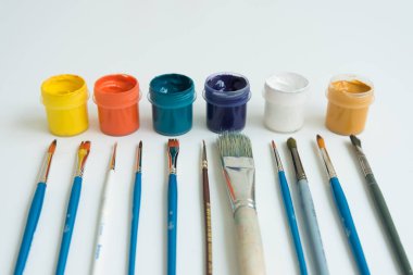 Kavanozlar dolusu guaj boyası farklı renklerde. Onun yanında çeşitli boyutlarda fırçalar var. Sanatçı kiti. Yan görüş. Beyaz arka plan. Hobiler ve ilham.