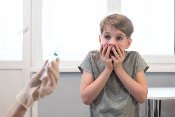 Das Kind schaut entsetzt auf die Spritze. Angst vor Spritzen. Emotionen, mangelnde Bereitschaft sich impfen zu lassen — Stockfoto