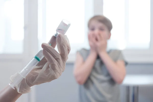 Das Kind schaut entsetzt auf die Spritze. Angst vor Spritzen. Emotionen, mangelnde Bereitschaft sich impfen zu lassen — Stockfoto