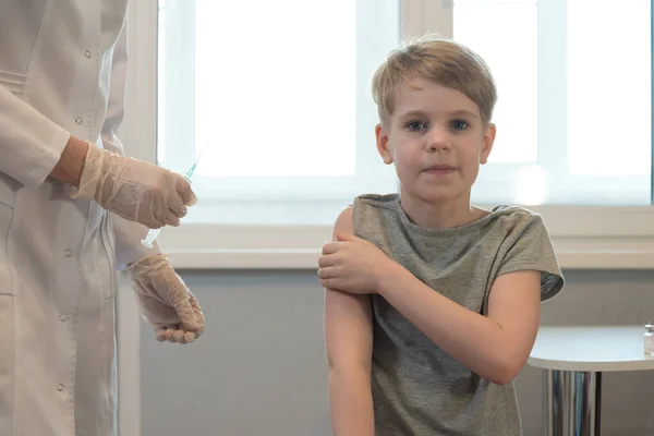 L'enfant sourit après l'injection, après la vaccination. Le médecin se tient à proximité, la seringue est visible. L'enfant regarde calmement la caméra et sourit — Photo