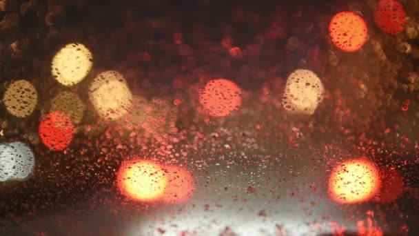Вид из машины на огни ночного города. Машина с подогревом лобового стекла. Машина в пробке, снег падает на стекло и тает. Дворник работает. Мягкий фокус фокусируясь на стекле — стоковое видео