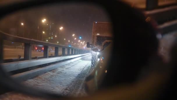 後ろのミラーは渋滞の中に立っている車を示しています。降雪による渋滞。冬の悪天候の概念。雪は大きなフレークの中に落ち — ストック動画