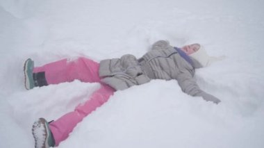 Çocuk zevkle karda yatıyor ve bir melek yapıyor. Çok fazla kar ve buz var. Mutlu çocukluk