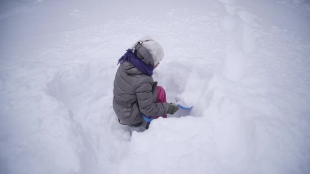 Το κορίτσι σκάβει το χιόνι. Το παιδί παίζει με πολύ χιόνι. Ένα ροδαλό παιδί στο κρύο. Ωραία βόλτα και παιχνίδι. — Αρχείο Βίντεο