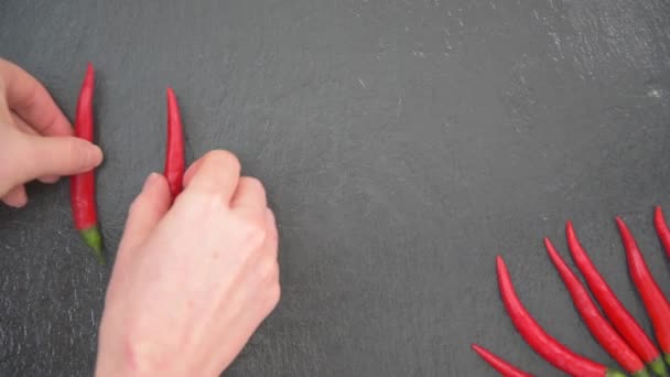 Женские руки распространяют слово "горячий" на доске. Красный перец чили. Чёрный фон — стоковое видео