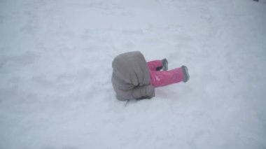 Gülen kız kar yığınlarında neşeyle yuvarlanıyor. Kış havası ve neşeli bir ruh hali. Gül gibi ve mutlu bir çocuk
