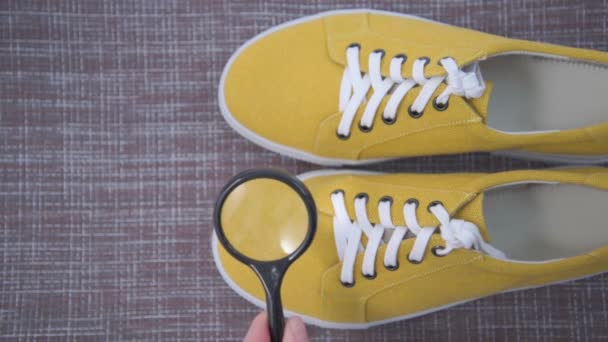 Inspection d'une paire de chaussures avec une loupe. Baskets en tissu jaune. Main avec une loupe dans le cadre. Inspection approfondie des chaussures — Video