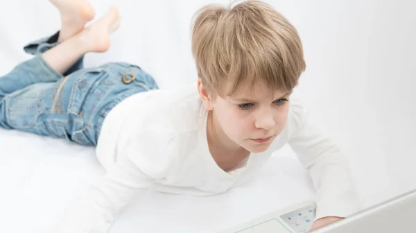 The blond child looks attentively at the computer or laptop screen. Close-up portrait — Stock Photo, Image