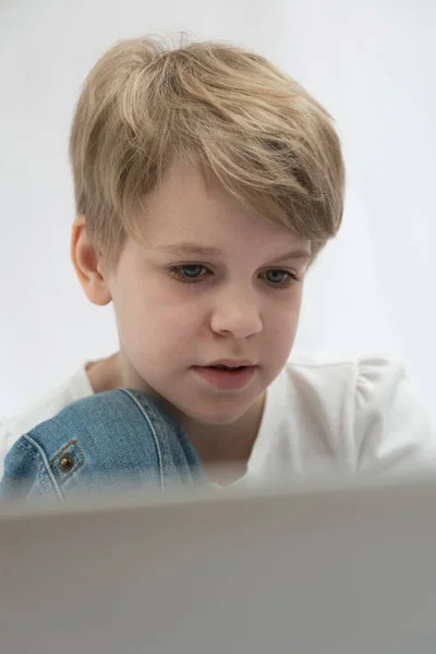 L'enfant blond regarde attentivement l'ordinateur ou l'écran d'ordinateur portable. Gros plan portrait — Photo