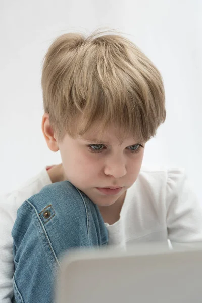 A criança loira olha atentamente para o computador ou a tela de computador portátil. Retrato de close-up — Fotografia de Stock