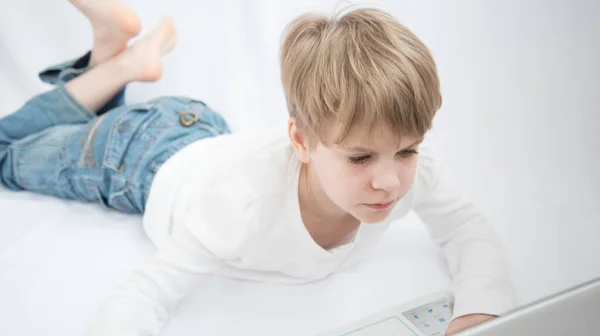 The blond child looks attentively at the computer or laptop screen. Close-up portrait — Stock Photo, Image