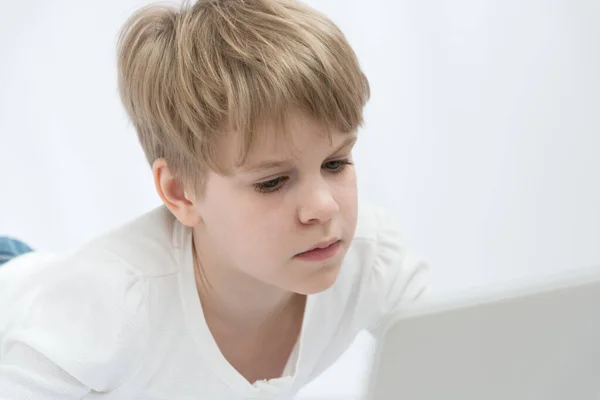 The blond child looks attentively at the computer or laptop screen. Close-up portrait — Stock Photo, Image