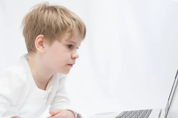 The blond child looks attentively at the computer or laptop screen. Close-up portrait — Stock Photo, Image