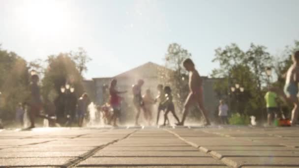 Zamazany obraz. Dzieci bawią się w fontannie. Odrzutowce fontanny pozwalają ochłodzić się w upalne lato. Słońce, zabawa i jasne kolory — Wideo stockowe