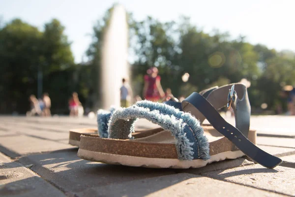 En primer plano están las sandalias ortopédicas para niños. Imagen borrosa en el fondo. Niños divirtiéndose en la fuente. Los chorros de la fuente le permiten refrescarse en los veranos calurosos. Sol, diversión — Foto de Stock