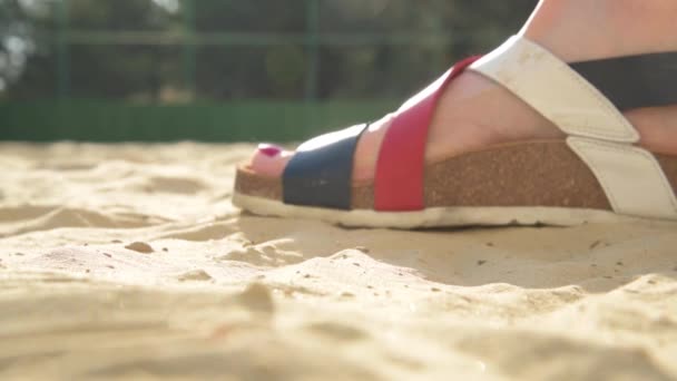 Kobiece stopy z bliska. Dziewczyna w ortopedycznych sandałach korkowych. Dziewczyna na plaży otwiera się, zdejmuje rzep na butach i chodzi boso po piasku. Koncepcja lata, wakacji, wolności — Wideo stockowe