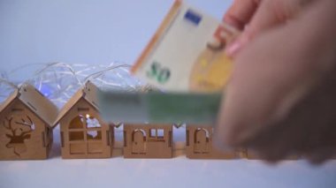 Avro faturalarını sayıp, evi satın almak için para ödüyorlar. Arka planda tahta oyuncak evler var. Ev satın alma konsepti. Konut sorununun çözümü