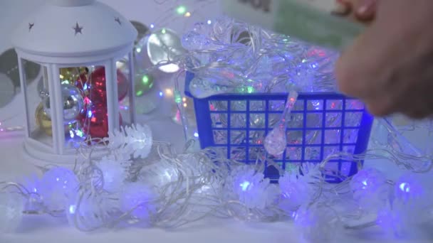 Primo piano di una mano di acquirenti. Il cliente seleziona le luci di Natale e le ispeziona sul bancone. Poi paga con le bollette dell'UE. Il concetto di scegliere le decorazioni per Natale e Capodanno — Video Stock