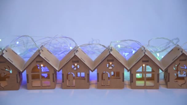 Krásné dřevěné věnec domy stojí v řadě. Za domem blikají vánoční světla a věnce. Nádherné kouzelné večerní osvětlení. Vánoční a novoroční koncepce přípravy. Domů — Stock video