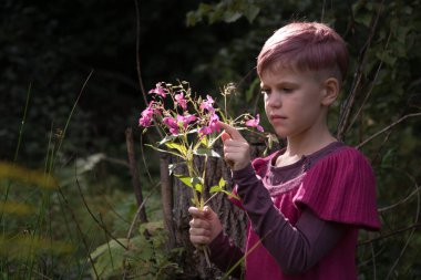Pembe elbiseli güzel bir kız bir buket çiçeği inceliyor. Doğayla çevrili bir çocuk. Pembe ve yeşil renklerin güzel bir kombinasyonu