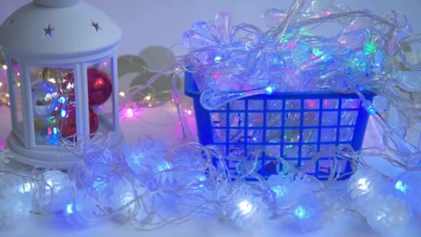 Guirnaldas de Navidad parpadeando con diferentes luces. Linterna con juguetes de Año Nuevo. Las guirnaldas están en una cesta. Concepto de preparación navideña — Vídeo de stock