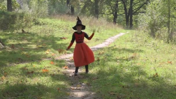 Bella ragazza vestita con un costume da strega per Halloween. La strega sta ballando. Il bambino sta ballando con foglie di quercia autunnale — Video Stock