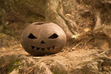 Cadılar Bayramı balkabağı kilden yapılır. Ağaç köklerinin arka planında korkunç korkunç bir balkabağı