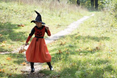 Cadılar Bayramı için cadı kostümü giymiş güzel bir kız. Cadı dans ediyor. Çocuk sonbahar meşe yapraklarıyla dans ediyor.