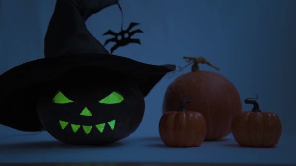 Halloween. Pumpkin with glowing eyes and a terrible smile. There is a blinking fire inside the pumpkin. A witchs hat is blown over the pumpkin — Stock Video