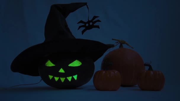 Halloween. Pumpa med glödande ögon och ett hemskt leende. Det är en blinkande eld inuti pumpan. En häxa hatt blåses över pumpa — Stockvideo