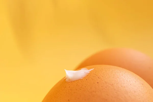 創造的な日焼け止めの概念 太もものような茶色の卵 フロントバトックにクリームのドロップ 壮大な影を持つ黄色の背景 ミニマリズムマクロ — ストック写真