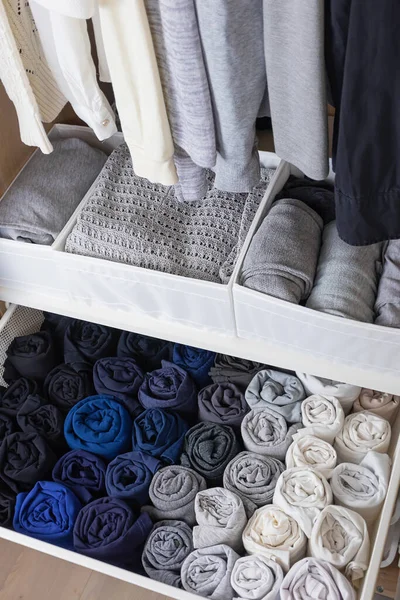 The concept of organizing space in the wardrobe. Clothes of dark and light shades hang neatly and lie in the closet.