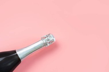 Pastel pembe arka planda gümüş folyolu şampanya şişesi boynu. Kutlama, tatil, yeni yıl konsepti. Minimalizm, boşluğu kopyala.