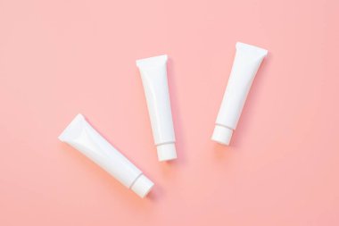 Pembe arka planda beyaz kozmetik tüpleri. Yüz ve vücut bakımı kavramı, kozmetik. Üst görünüm, minimalizm, düz görünüm, kopyalama alanı.
