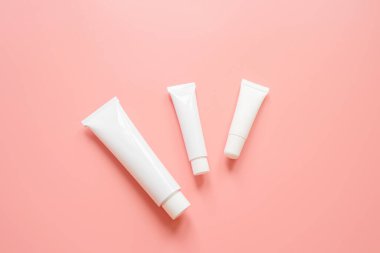 Pembe arka planda beyaz kozmetik tüpleri. Yüz ve vücut bakımı kavramı, kozmetik. Üst görünüm, minimalizm, düz görünüm, kopyalama alanı.
