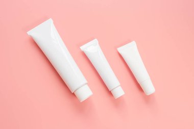Pembe arka planda beyaz kozmetik tüpleri. Yüz ve vücut bakımı kavramı, kozmetik. Üst görünüm, minimalizm, düz görünüm, kopyalama alanı.