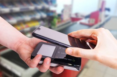 Pos terminalleri ve akıllı telefon. Arka planda bir süpermarket kasası var. Banka ekipmanları. Ediniyorum. Banka kredi kartlarının kabul edilmesi. Temassız ödeme.