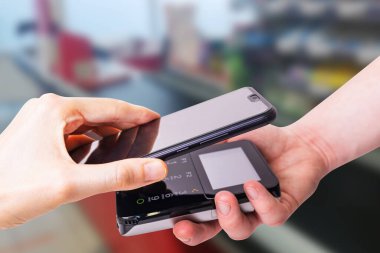 Pos terminalleri ve akıllı telefon. Arka planda bir süpermarket kasası var. Banka ekipmanları. Ediniyorum. Banka kredi kartlarının kabul edilmesi. Temassız ödeme.