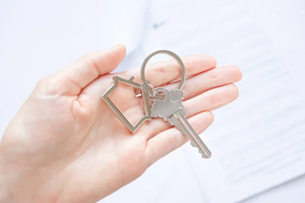闭锁的钥匙与房子形状的钥匙链在掌心 文件在背后 购买和担保房地产 抵押贷款的概念 复制空间 — 图库照片
