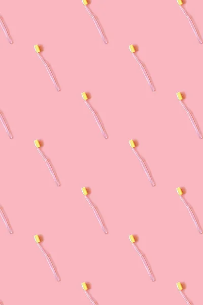 Toothbrushes with yellow bristles on a pink background. Pattern. Oral hygiene, dentistry, teeth cleaning concept. Minimalism, top view, copy space.