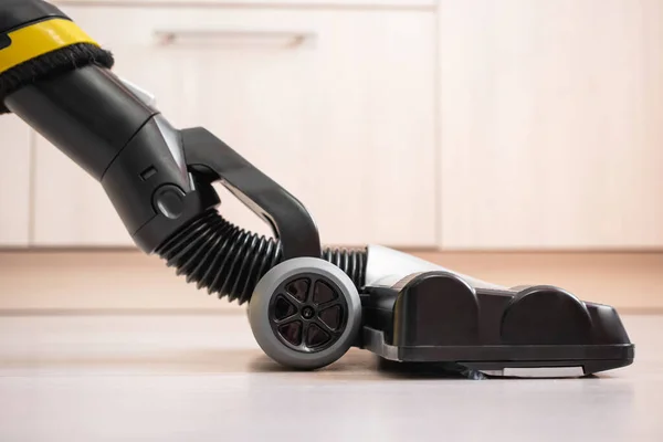 Upright vacuum cleaner brush on the laminate floor close-up. In the background are lockers. Beige, gray and yellow shades. House cleaning concept.